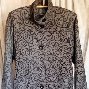 May include: A long-sleeved gray jacket with a black floral pattern. The jacket has a mandarin collar and four black buttons down the front.