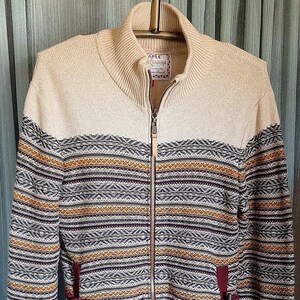 May include: A zip-up sweater with a cream-colored upper section and a patterned lower section. The pattern includes horizontal stripes in shades of brown, gold, and burgundy. The sweater has a high collar and two pockets. The label reads "APLE".