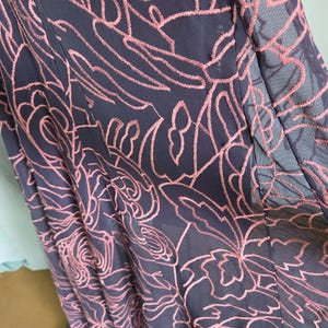 May include: Close-up of navy blue fabric with pink floral embroidery. The embroidery forms a delicate, textured pattern across the material. The fabric appears to be part of a dress or skirt.