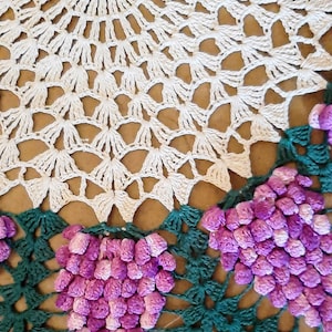 May include: A white crocheted doily with a green crocheted border and purple crocheted grapes.