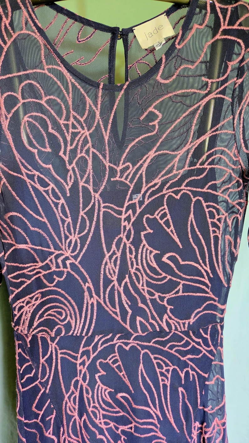 May include: Navy blue dress with pink floral embroidery. The dress has a round neckline and long sleeves. The brand tag "jade" is visible at the neckline.