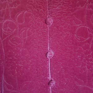 Puede incluir: Chaqueta de terciopelo magenta con un patr&oacute;n floral acolchado y cuello mandar&iacute;n. La chaqueta tiene cierre de botones con cuatro botones forrados de tela a juego. La tela tiene un brillo sutil.