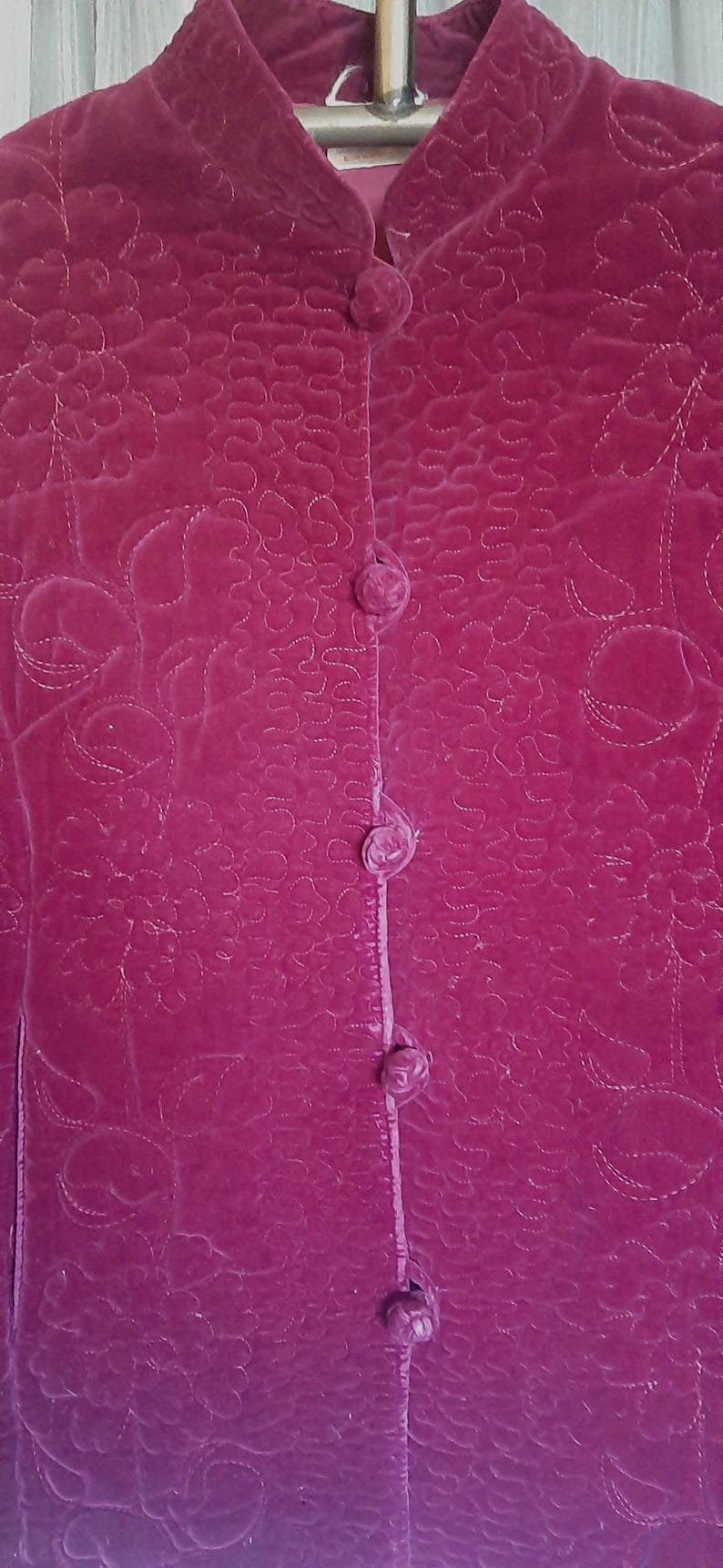 Puede incluir: Chaqueta de terciopelo magenta con un patr&oacute;n floral acolchado y cuello mandar&iacute;n. La chaqueta tiene cierre de botones con cuatro botones forrados de tela a juego. La tela tiene un brillo sutil.