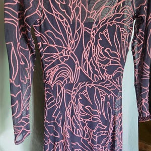 May include: Navy blue dress with a pink floral pattern overlay. The dress has long sleeves and a keyhole neckline. The overlay is a sheer mesh, creating a layered effect. The dress is a midi length.