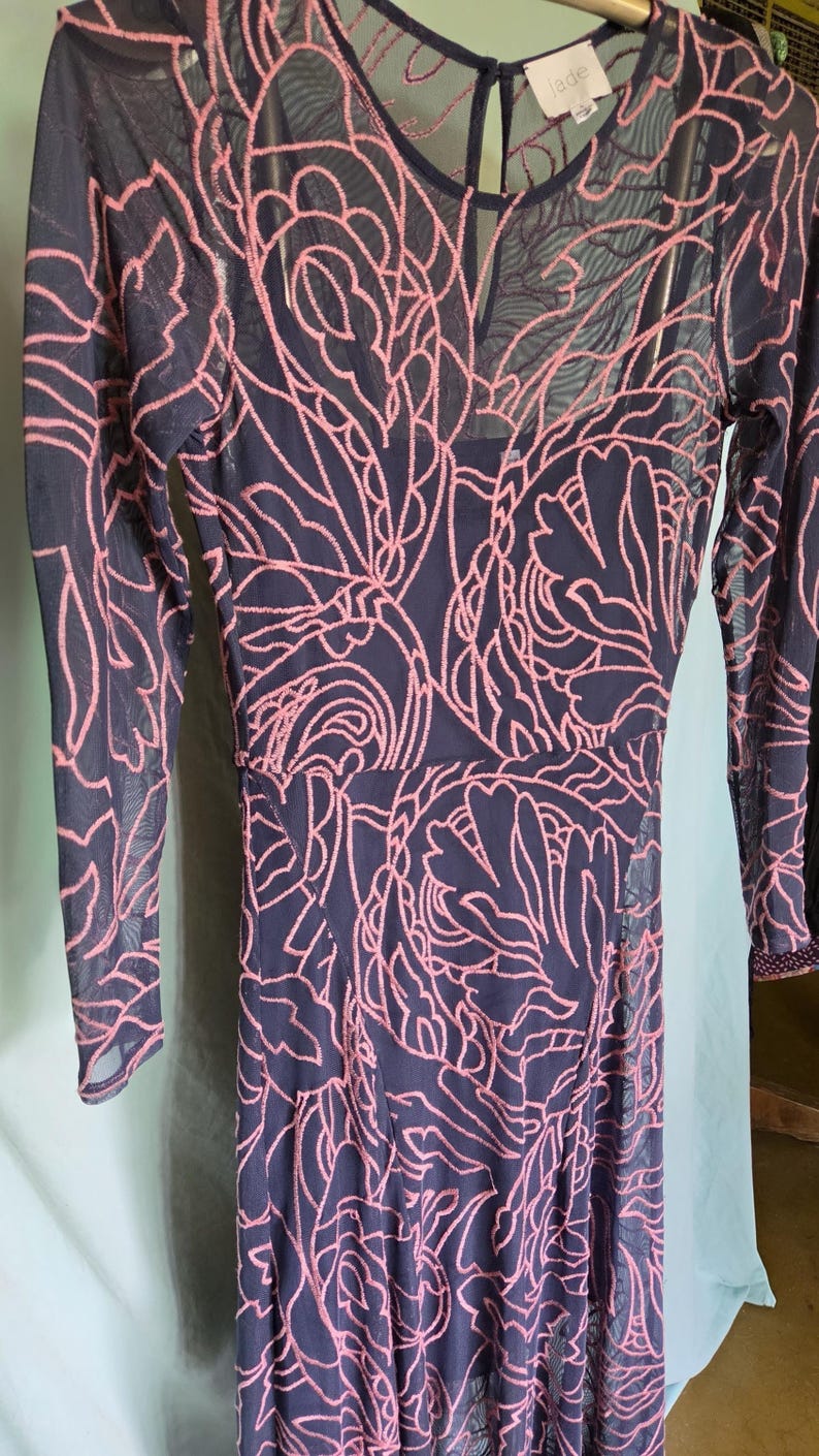 May include: Navy blue dress with a pink floral pattern overlay. The dress has long sleeves and a keyhole neckline. The overlay is a sheer mesh, creating a layered effect. The dress is a midi length.