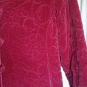 Puede incluir: Chaqueta de terciopelo burdeos con estampado floral. La chaqueta presenta un dise&ntilde;o acolchado con cierre de botones y mangas largas. El estampado floral est&aacute; cosido con hilo blanco.