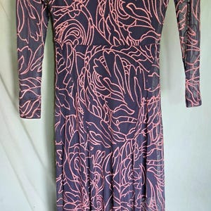 May include: A navy blue maxi dress with a sheer pink floral pattern overlay. The dress has long sleeves and a scoop neck. The label reads "jade".