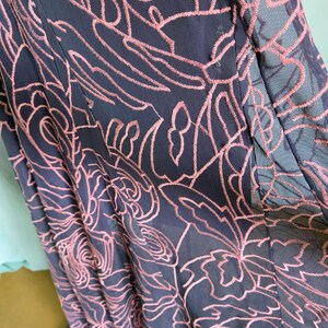 May include: Close-up of a navy blue dress with a floral pattern embroidered in a light pink colour. The dress has a sheer overlay, and the embroidery creates a textured effect.