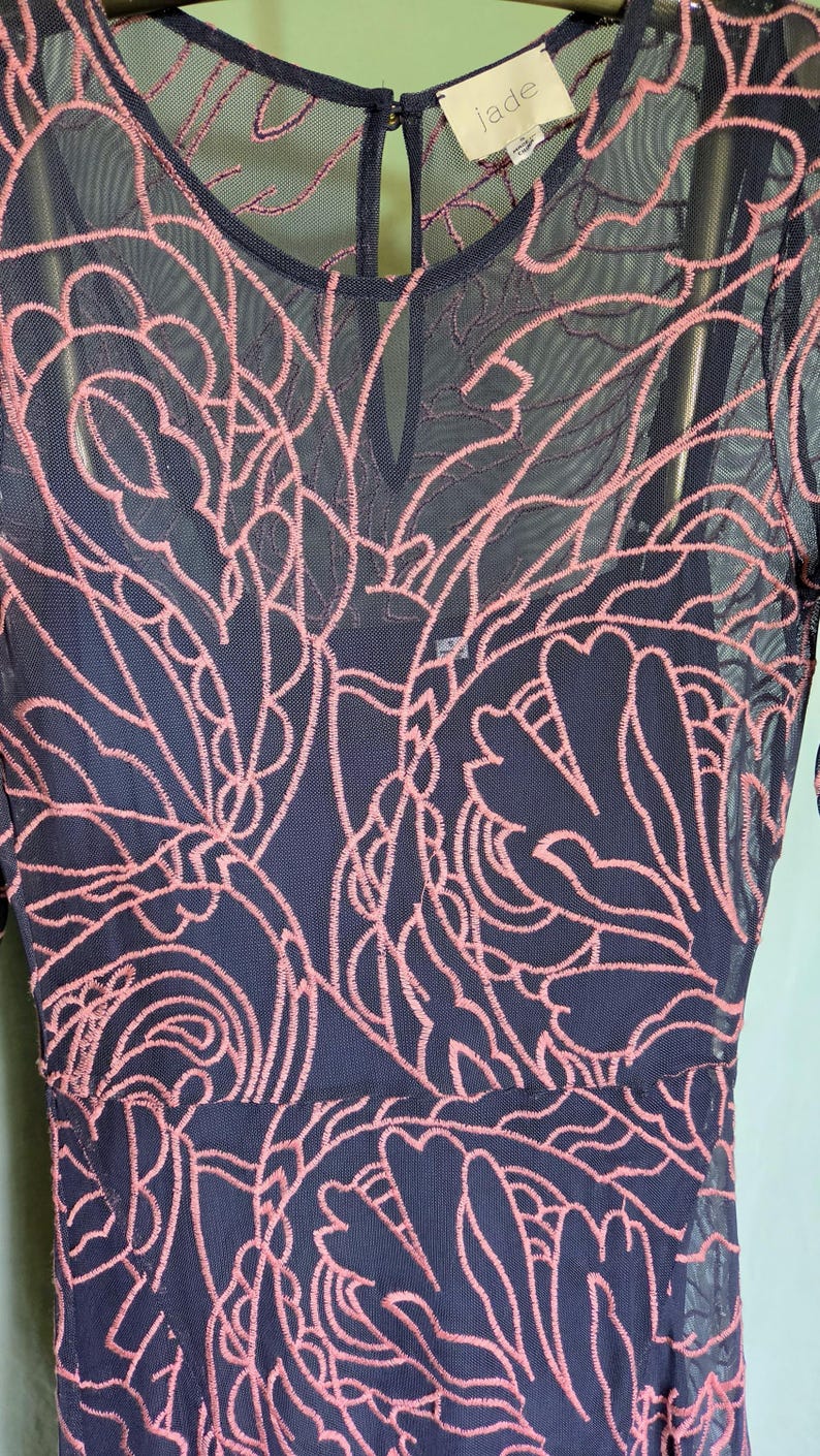 May include: A navy blue dress with a pink floral lace overlay. The dress has a round neckline and long sleeves. The brand label "jade" is visible at the neckline.