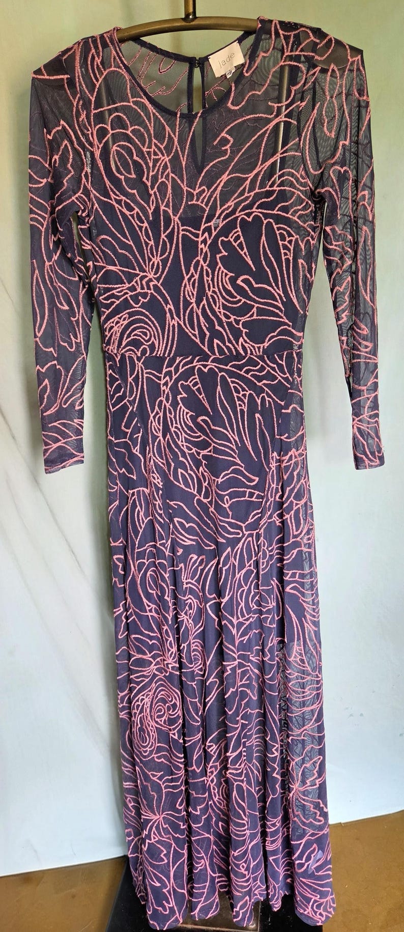 May include: A navy blue dress with a pink floral design and long sleeves. The dress has a sheer overlay, a round neckline, and a flowing skirt. The label reads "jade".