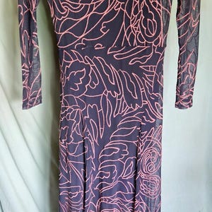May include: A long, dark blue dress with a pink floral pattern. The dress has long sleeves and a sheer overlay. The floral design is intricate and covers the entire dress. The dress is floor-length and appears to be made of a lightweight material.