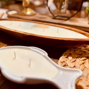 May include: Two white candles in wooden and ceramic holders. The wooden holder is shaped like a boat and the ceramic holder is shaped like a fish. Both candles have wicks.