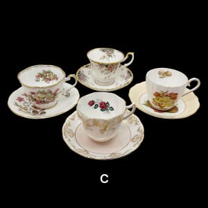May include: Four vintage teacups and saucers are displayed against a black background. Each cup features a unique floral design with gold trim. The saucers complement the cups with matching patterns and colors, creating an elegant tea set.