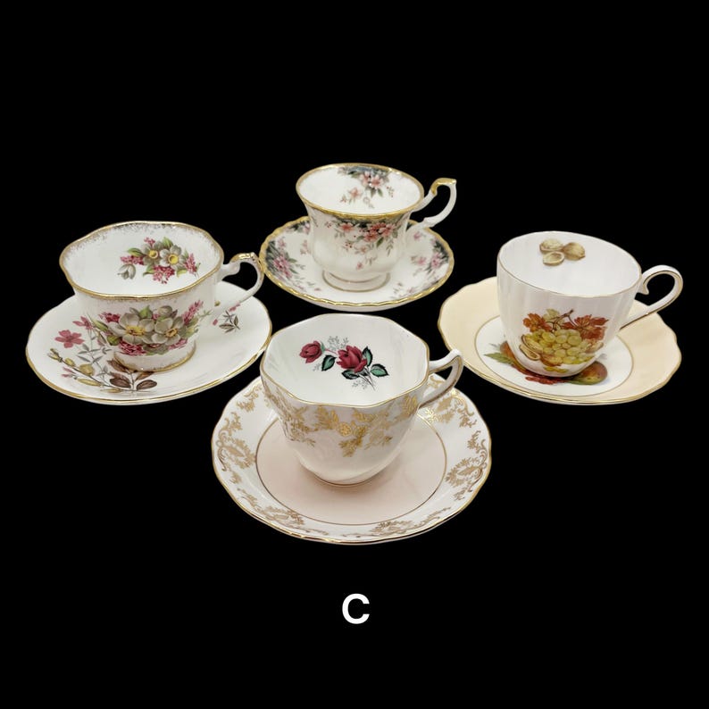 May include: Four vintage teacups and saucers are displayed against a black background. Each cup features a unique floral design with gold trim. The saucers complement the cups with matching patterns and colors, creating an elegant tea set.