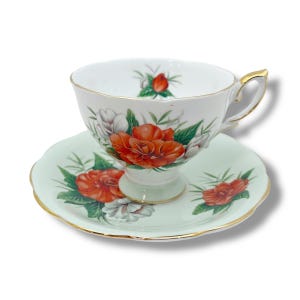 Puede incluir: Un juego de taza y platillo de té blanco con fondo verde y diseño floral rojo y blanco.