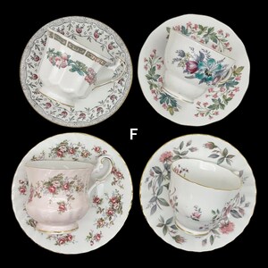 May include: Four vintage teacups and saucers with floral patterns. The teacups are white with pink and green floral designs, and gold trim. The saucers have matching floral patterns and gold rims. The teacups are arranged on a black background.