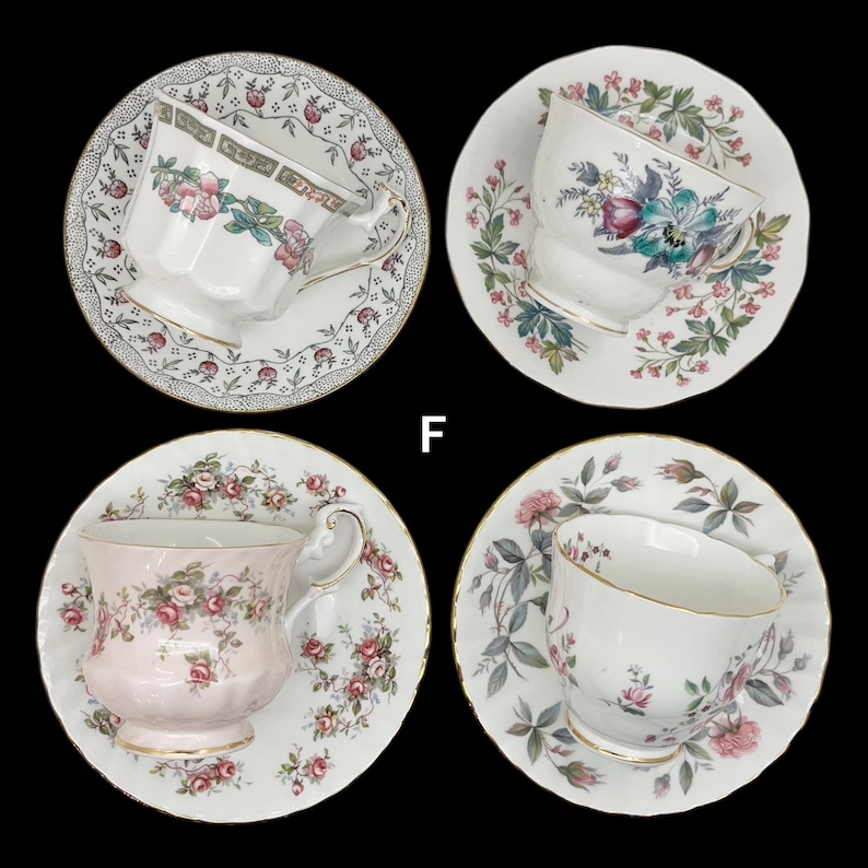 May include: Four vintage teacups and saucers with floral patterns. The teacups are white with pink and green floral designs, and gold trim. The saucers have matching floral patterns and gold rims. The teacups are arranged on a black background.