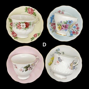 May include: Four vintage teacups and saucers are displayed against a black background. Each teacup features a different floral design, with colors including pink, red, blue, and yellow. The saucers are in matching colors.