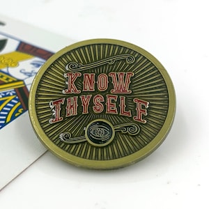 May include: A gold-colored round pin with the words "Know Thyself" in red lettering. The pin has a black eye design in the center.