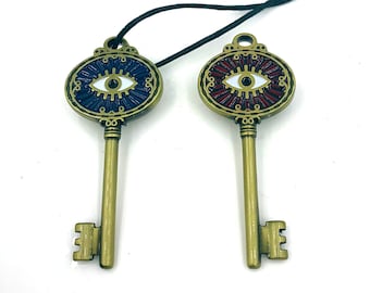 May include: Two gold-tone keychains with an eye design. One eye is blue and white, the other is red and white. Both keychains have a black cord.