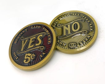 Può includere: Due monete di metallo color oro con un design a raggiera. Una moneta ha la parola "YES" in lettere rosse e dorate e il testo "DESTINY FATE FORTUNE" attorno al bordo. L'altra moneta ha la parola "NO" in lettere dorate e il testo "ALL KNOW ALL TELL ALL" attorno al bordo.