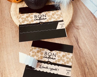 Könnte beinhalten: Zwei schwarze Geschenkkarten mit goldenen Akzenten und einem braunen Musterhintergrund. Der Text auf den Karten lautet "BON cadeau" und "La famille s'agrandit!" mit den Worten "OUVRIR ici" auf beiden Karten.
