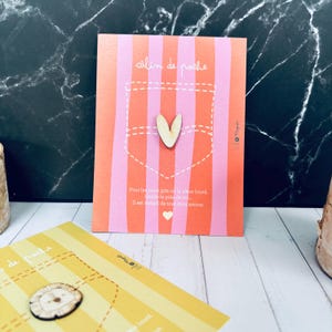 Peut inclure: Une carte à rayures roses et oranges, avec un motif de poche et un cœur en bois. Le texte "calin de poche" est en haut. Du texte supplémentaire est en bas. Une deuxième carte avec un lion en bois est également visible.