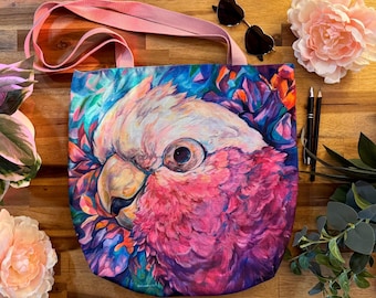 Può includere: Una borsa tote rosa con la stampa di un cacatua rosa e bianco su uno sfondo floreale blu, viola e verde.