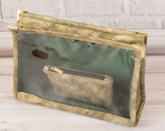 Puede incluir: Una bolsa de cremallera dorada con un frente de plástico transparente. La bolsa está sobre una superficie de madera clara.