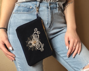 May include: A dark blue velvet clutch with a gold embroidered spider web design. The clutch is attached to a gold chain.