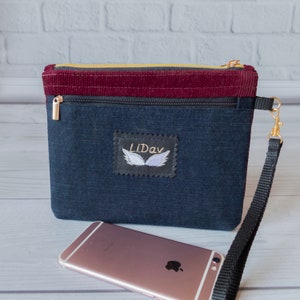 May include: A dark blue denim zippered pouch with a burgundy corduroy top. The pouch has a black strap and a small embroidered patch with the text "LiDav" and a pair of wings.