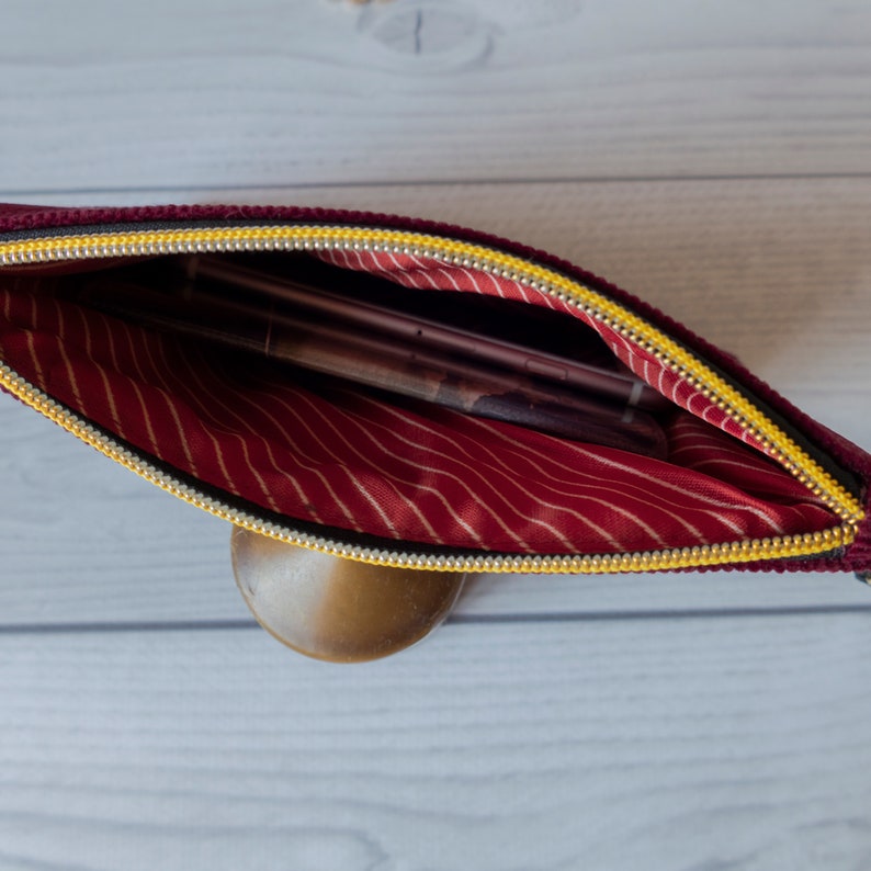 May include: A burgundy velvet zippered pouch with a yellow zipper and a red and white striped lining. The pouch is open and contains several items.