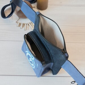May include: A blue canvas fanny pack with a zippered pocket and a blue and white design. The fanny pack is open and the inside is visible.