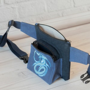 May include: A blue fanny pack with a zippered pocket and a dragon design. The pack has a detachable strap.
