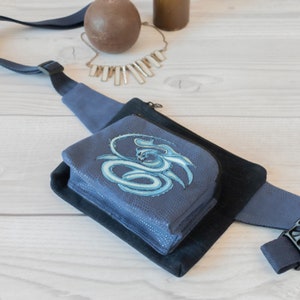 May include: A blue and black fanny pack with a zipper closure and a blue dragon design on the front. The fanny pack is made of a soft, textured material.