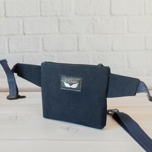 May include: A dark blue denim fanny pack with a zipper closure and a white embroidered wing logo that says "Lidav".