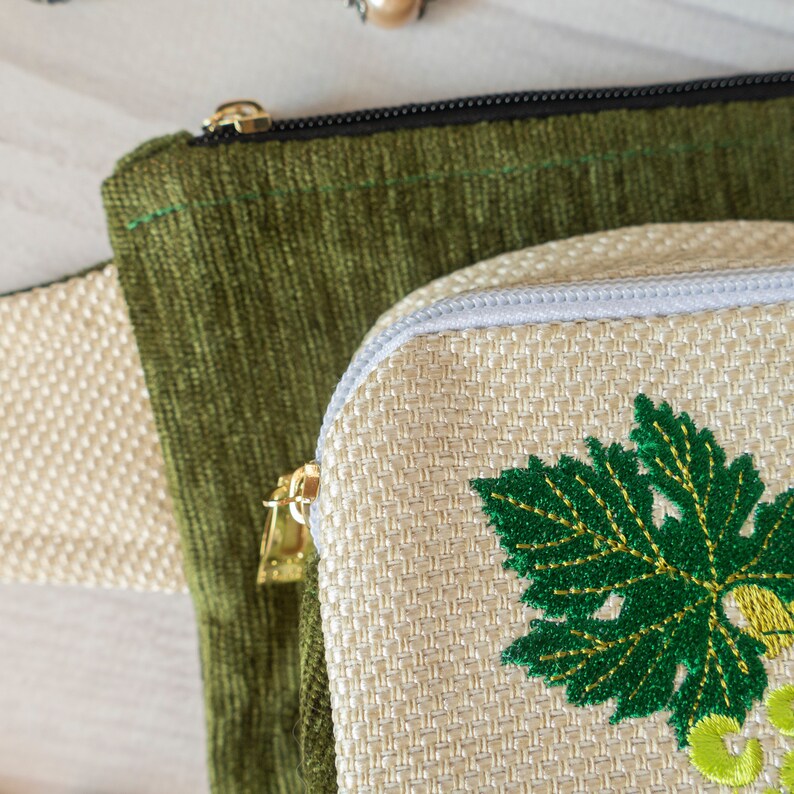 May include: Two fabric pouches, one green and one beige. The beige pouch has a green embroidered leaf design.