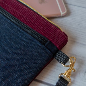 May include: A small blue denim and burgundy corduroy zippered pouch with a gold zipper and a black strap with a gold clasp.
