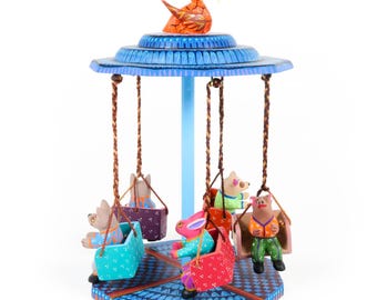May include: A colourful wooden carousel with a blue base and a bright orange swan on top. Five painted animal figures ride on swings around the carousel.