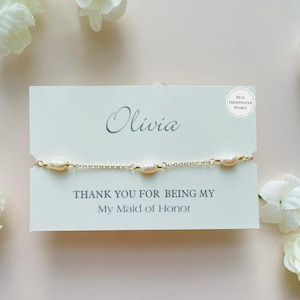 May include: A gold-colored chain bracelet with three oval freshwater pearls. The bracelet is displayed on a card that reads "Olivia" and "Thank you for being my My Maid of Honor."
