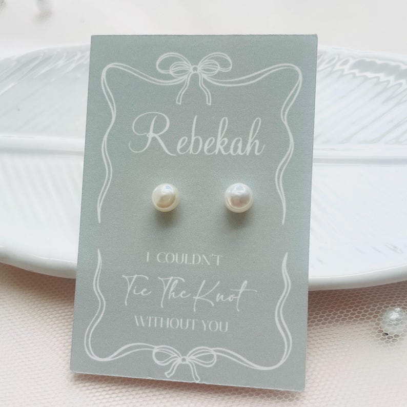 May include: Pearl stud earrings presented on a pale blue card. The card is inscribed with the name "Rebekah" and the message "I Couldn't Tie The Knot Without You", with decorative bow illustrations.