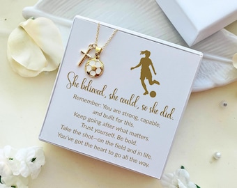 Könnte beinhalten: Eine goldfarbene Halskette mit einem Fußballanhänger und einem Kreuz, präsentiert auf einer weißen Schachtel mit goldenem Text. Auf der Schachtel steht "She believed, she could, so she did." und eine Silhouette einer Fußballspielerin.