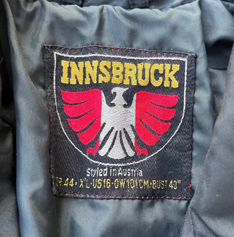 May include: Black and red patch with white stitching. The patch has a white eagle with red wings and the text "INNSBRUCK" in yellow letters. The text "styled in Austria" and "GR.44, XL-US 16-OW 101CM-BUST 40" is also on the patch.