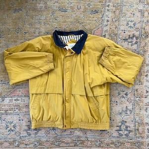 May include: A mustard yellow jacket with a navy blue and white striped collar. The jacket has a zipper closure and two pockets on the front.