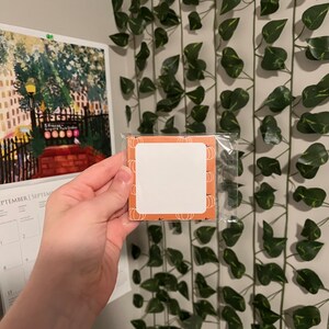 Könnte beinhalten: Ein kleiner, quadratischer, orangefarbener und weißer Notizblock mit einem weißen Bereich zum Schreiben. Der Notizblock hat ein Kürbisdesign und befindet sich in einer durchsichtigen Plastiktüte.