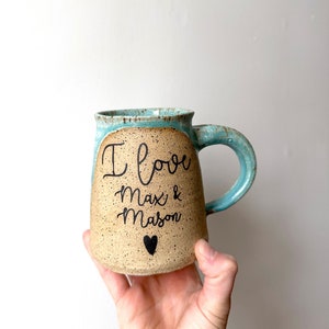 May include: A light blue and brown ceramic mug with the text "I love Max & Mason" and a small black heart.