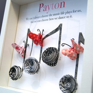 May include: A white framed picture with the name "Payton" written in pink at the top. The quote "We can't always choose the music life plays for us, but we can choose how we dance to it." is written below the name. The picture features black and white paper flowers and red and white paper butterflies.