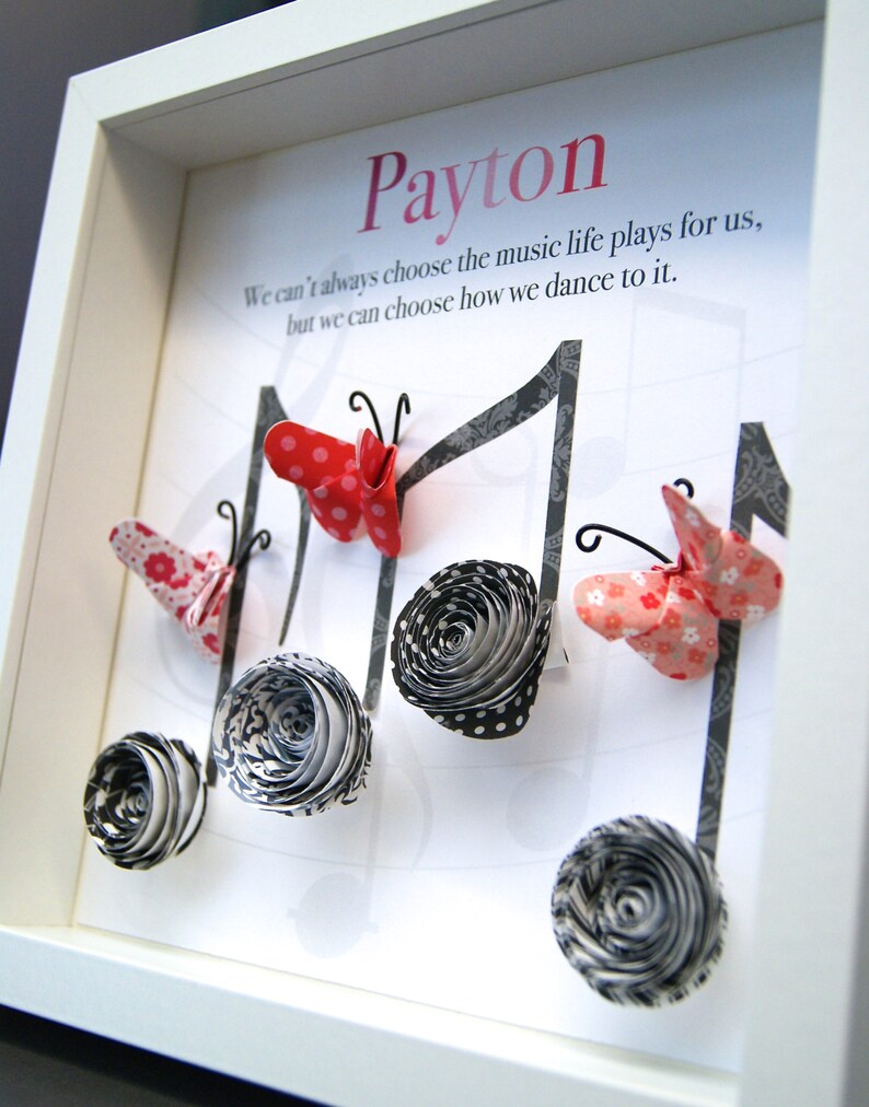 May include: A white framed picture with the name "Payton" written in pink at the top. The quote "We can't always choose the music life plays for us, but we can choose how we dance to it." is written below the name. The picture features black and white paper flowers and red and white paper butterflies.