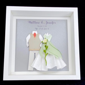 Peut inclure: Un cadre blanc avec un fond gris repr&eacute;sentant une d&eacute;coupe en papier d'un couple en tenue de mariage. Le texte "Matthew & Jennifer" et "December 17, 2021" est &eacute;crit en violet. Le texte "Yes, I am for it" est &eacute;crit en violet sous la date.
