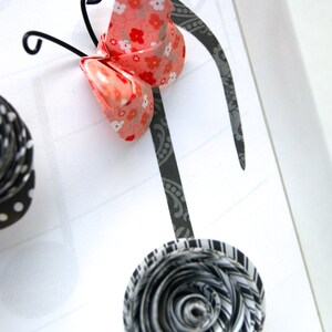 May include: A black and white paper flower with a black and white patterned background. A pink and white butterfly with a floral pattern is attached to a black musical note.